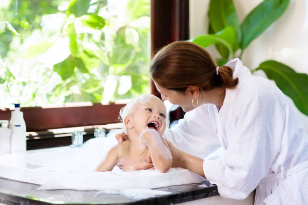 Mother washing baby in bubble bath. Water fun. Little child taking bubble bath in beautiful bathroom with big garden view window. Mother washing baby. Kids hygiene. Shampoo, hair treatment and soap foam for children. Mom bathing kid in large tub. girls bath stock pictures, royalty-free photos & images