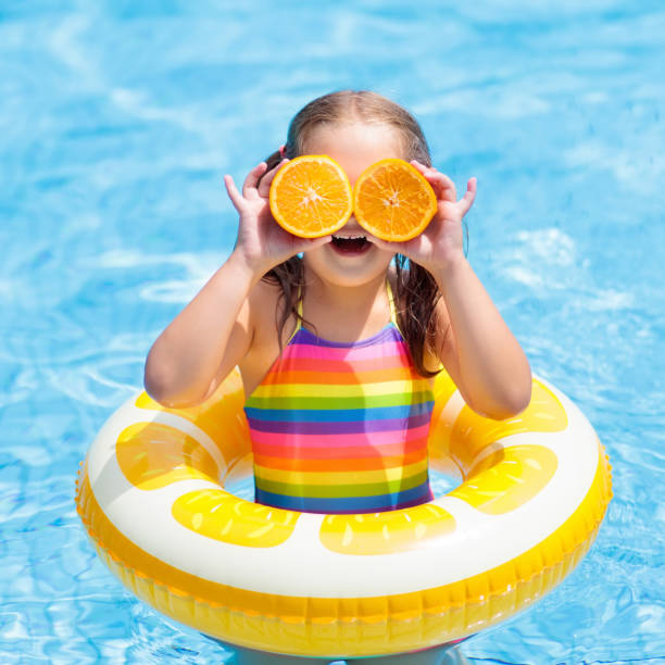 istock Child in swimming pool. Kid eating orange. 945297404