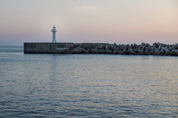 istock Seawall with wavebreakers with white lighthouse during dawn in Seogwipo, Jeju Island, South Korea 945330520