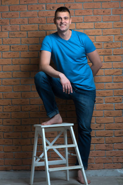 istock brutal barefoot man in a chair posing against a brick wall background 945343316