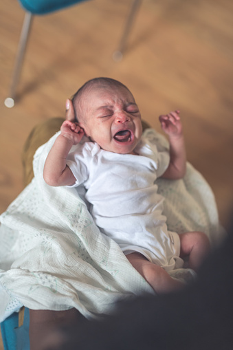 Overhead view of an African American mom as she gently cradles her newborn daughter in her arms...who is screaming and has her eyes closed and arms raised by her head. Time to eat?