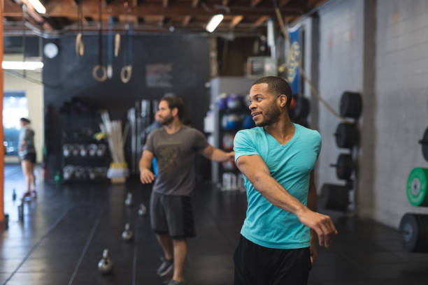 Small group working out in a modern health club Several people work out in a modern, open gym. Two males in the foreground are doing stretching exercises and swiveling their torsos and swinging their arms side to side. community health center stock pictures, royalty-free photos & images