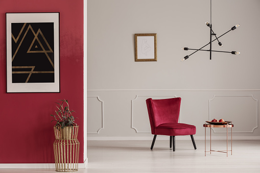 Gold table against red wall with black poster in apartment interior with armchair against white wall