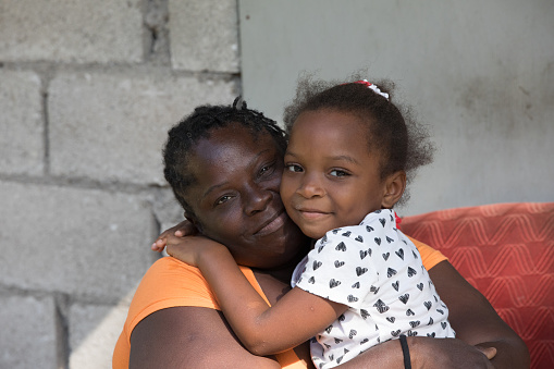 Jamaican mother sits in a chair outside hugging her  young daughter. Shot with Canon 5D Mark lV.
