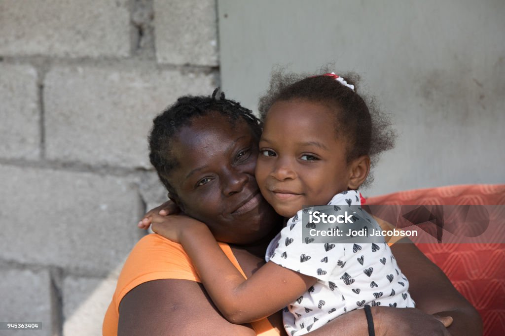 Portrait of a Jamaican mother from a remote village hugging her young daughter Jamaican mother sits in a chair outside hugging her  young daughter. Shot with Canon 5D Mark lV. Poverty Stock Photo