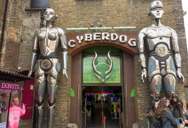 London, United Kingdom — March 23, 2018: People gather in front of the giant robots at the entrance of Cyberdog, a trance music and cyber clothing store in Camden Market. Alternative fashion store Cyberdog in Camden Market dubstep photos stock pictures, royalty-free photos & images