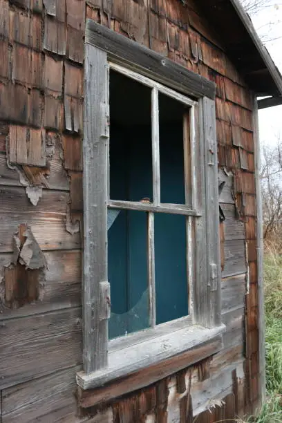 A four-paned window in an abandoned home with wooden shingle siding.