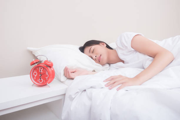 istock Young woman sleeping in bed beside alarm clock 945380834