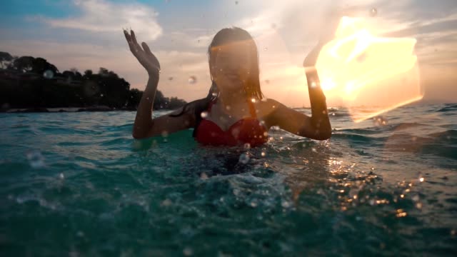 Asian sexy girl in bikini with wet hair and lips Having Fun Splashing in the sunset at sea