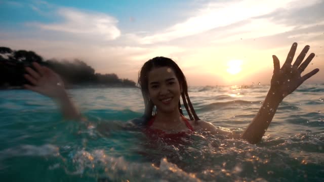 Asian sexy girl in bikini with wet hair and lips Having Fun Splashing in the sunset at sea