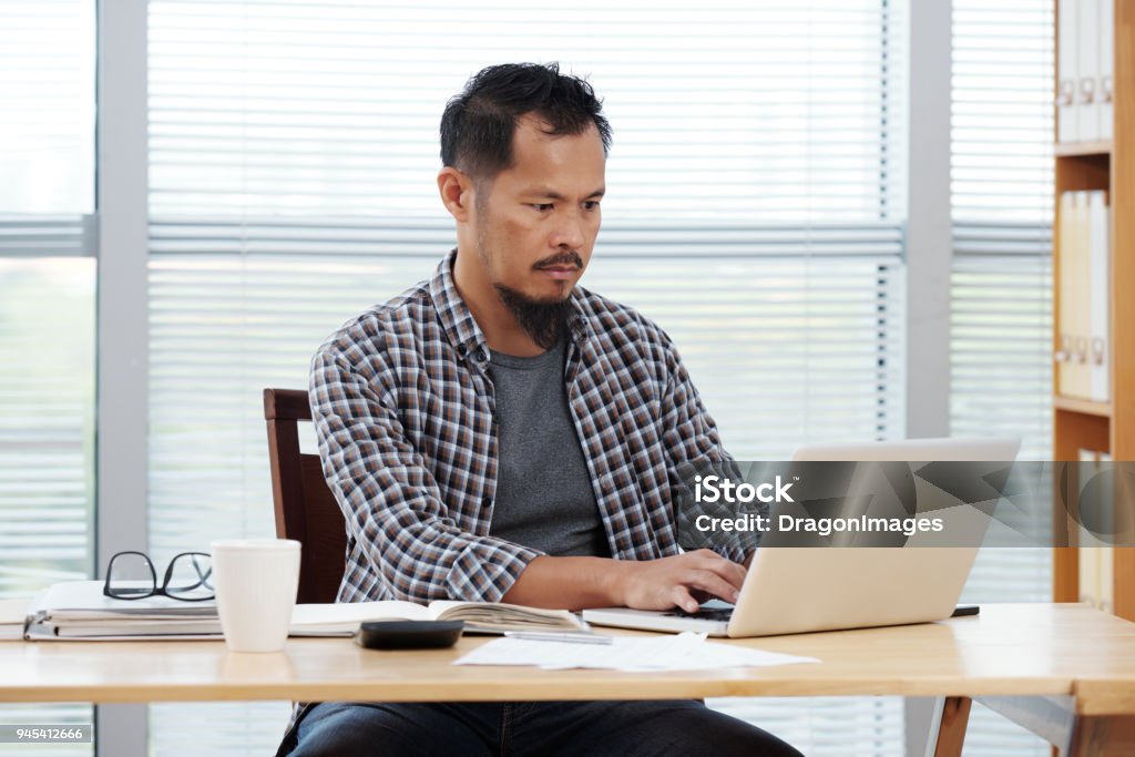Busy with work Filipino entrepreneur working on laptop in his office Adult Stock Photo