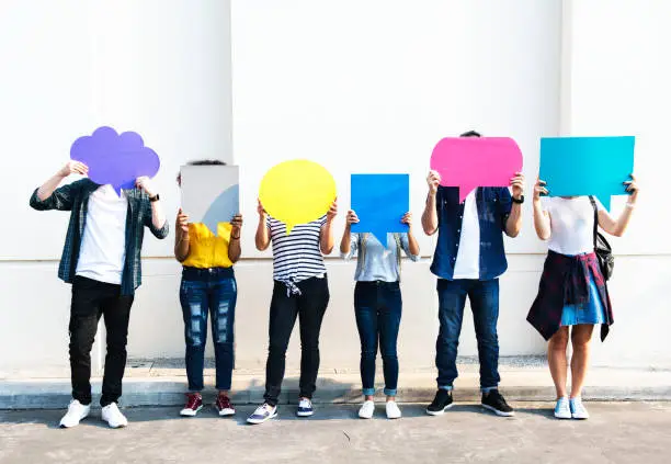 Photo of Young adult friends holding up copy space placard thought bubbles
