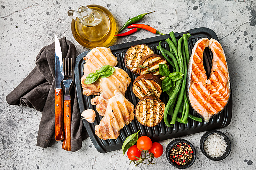 healthy food - grilled salmon steak, chicken and vegetables over gray background, top view