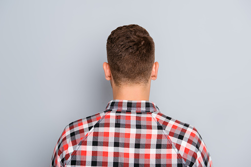 Back view of young guy in chekered shirt on gray background