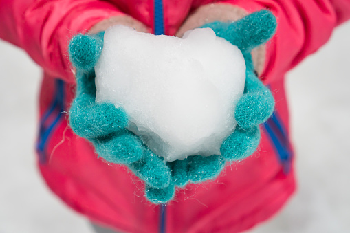 Child wearing winter gloves holding icy snow heart in hands