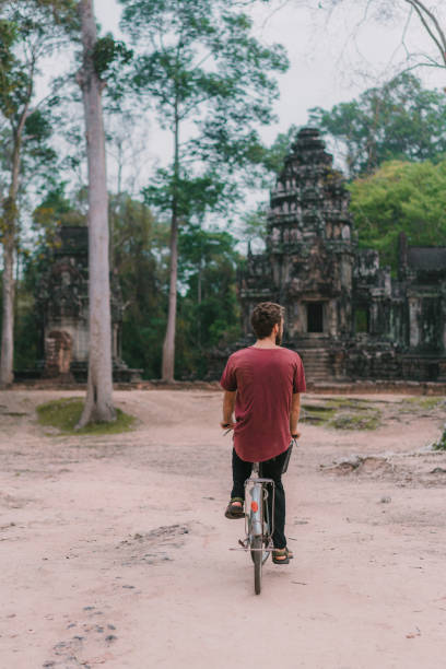istock Young Caucasian man riding  bicycle  in Angkor Wat 945440398