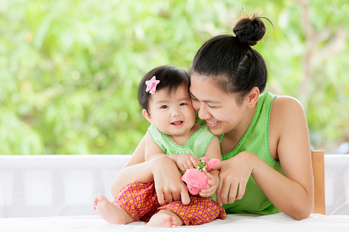 Cute asian baby girl in Thai traditon dress smiling and playing with her mother and turtle doll with love and happiness