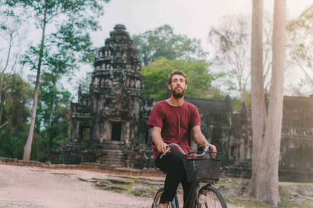 istock Young Caucasian man riding  bicycle  in Angkor Wat 945447314