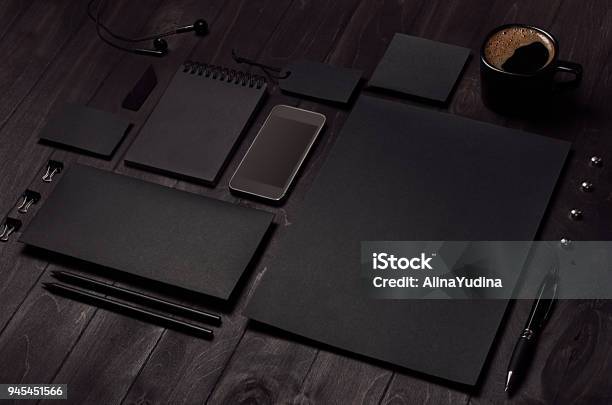 Black Blank Stationery Set With Phone Earphone Coffee On Dark Wood Background Inclined Stock Photo - Download Image Now