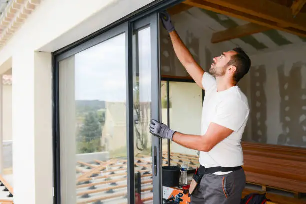 Photo of handsome young man installing bay window in a new house construction site