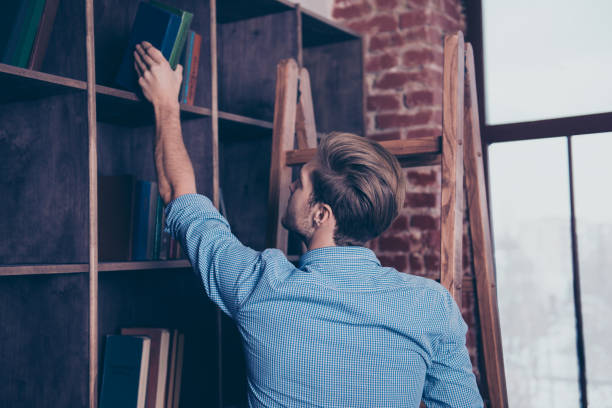 istock Young man in blue shirt in library searching for book 945461672