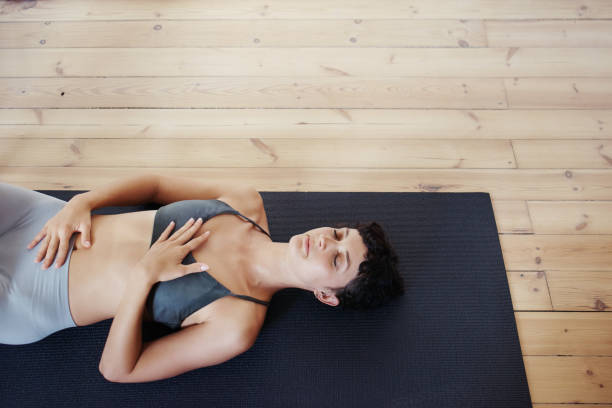 Feeling calm and content after her yoga session Shot of a beautiful young woman doing yoga at home lying on back stock pictures, royalty-free photos & images