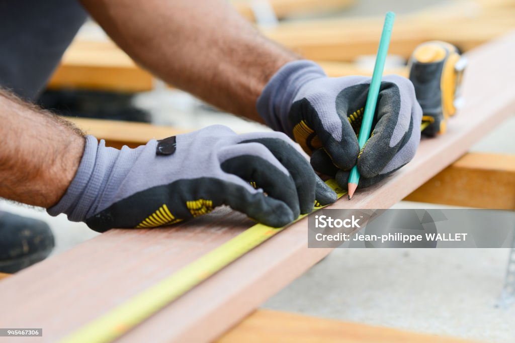 close up detail of manual worker hands working with a measuring tape and pencil in wood plank Carpenter Stock Photo