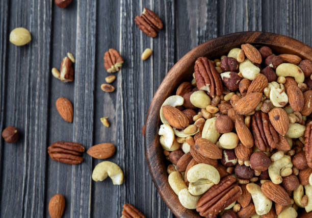 istock Nuts mix Almonds, Cashews, Macadamia, Peanuts, Walnuts, Pecans, Pine Nuts, Pistachios in a wooden plate 945470676