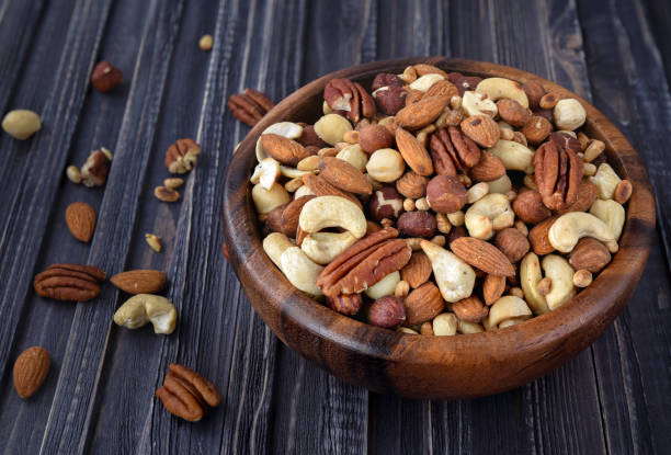 istock Nuts mix Almonds, Cashews, Macadamia, Peanuts, Walnuts, Pecans, Pine Nuts, Pistachios in a wooden plate 945470812