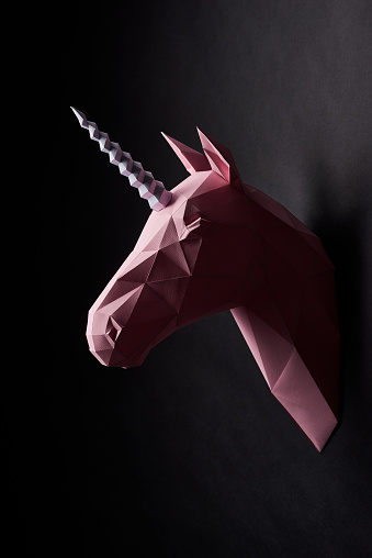 Pink powder coloured unicorn's head profile hanging on dark black smooth wall. Horse has intresting geometrical shape and straight lines. Original decoration for modern design. Interesting details.
