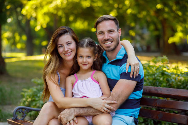 istock Little girl with parents sitting on park bench 945486768