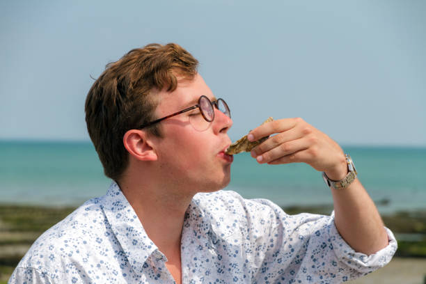 Oyster tasting Young man enjoys the taste of fresh raw oysters at the French coast of Brittany (Bretagne) in Cancale, France on a summer day cancale photos stock pictures, royalty-free photos & images