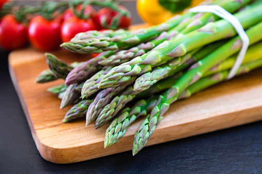 Bunch of fresh green asparagus on a wooden cutting board in the kitchen. Asparagus is a healthy vegetable high in vitamin K and antioxidants.