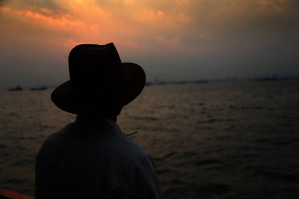 Old man of Indian ethnicity enjoying summer vacation on nautical vessel in the sea. Ferry boat start to travel. A ferry is a merchant vessel used to carry passengers, and sometimes vehicles and cargo as well, across a body of water.