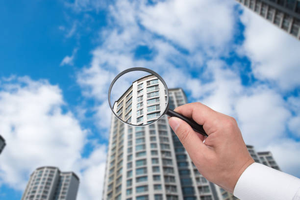 A hand holding a magnifying glass against the backdrop of an apartment. stock photo