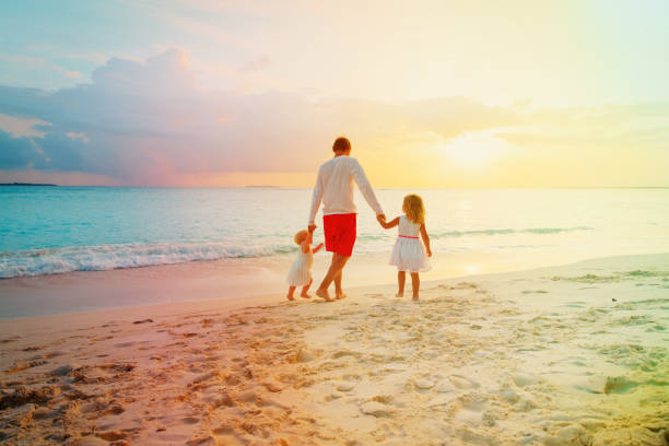 father with two kids walking on beach at sunset, parenting