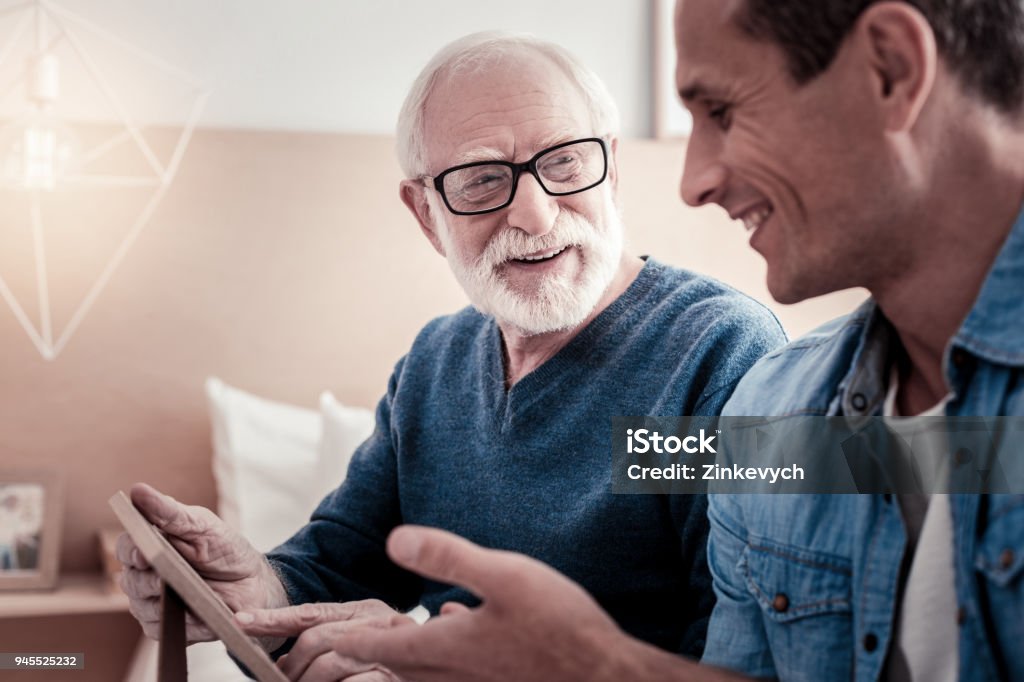 Cheerful nice man talking to his grandfather Pleasant communication. Cheerful nice pleasant smiling and talking to his grandfather while spending time with him Senior Adult Stock Photo