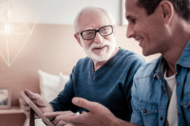 Cheerful nice man talking to his grandfather Pleasant communication. Cheerful nice pleasant smiling and talking to his grandfather while spending time with him memories stock pictures, royalty-free photos & images