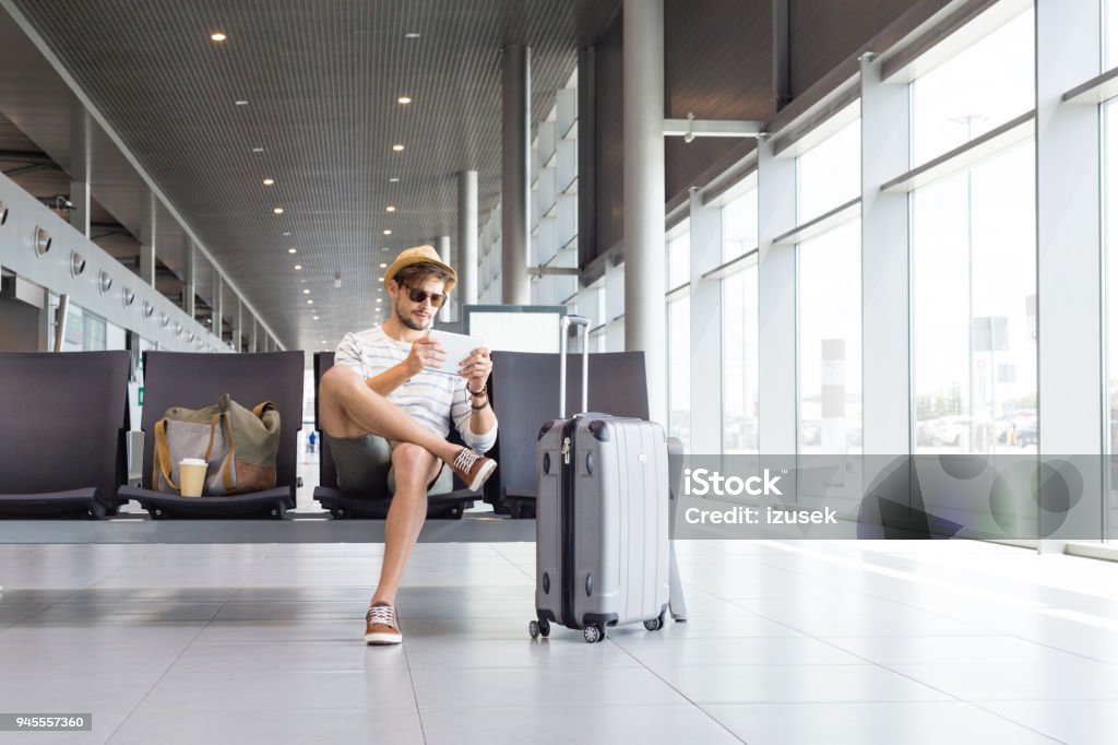 Man using digital tablet in airport lounge Handsome young man using digital tablet in airport lounge. Caucasian male passenger waiting for flight at airport terminal. Adult Stock Photo