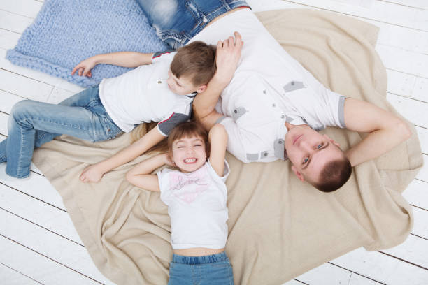 istock Father with his two little children lying at floor and having fun. Looking at camera. 945587608