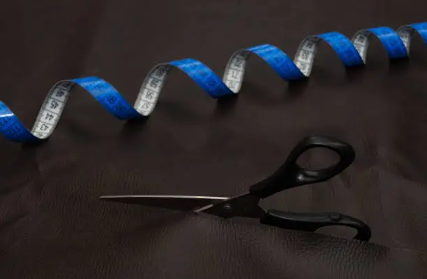 Concept of leather cutting-out. Black scissors and blue twisted tape measure