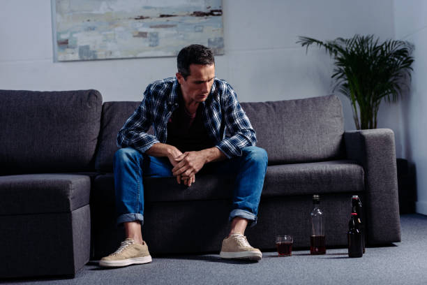 istock man looking at alcohol on floor while sitting on sofa at home 945640026