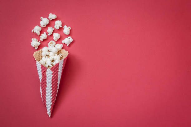 istock High angle view of cone with popcorn on red background minimalistic concept. 945652086
