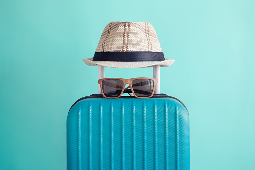 Suitcase with hat and sunglasses on pastel green background minimal creative travel concept