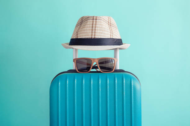 багаж с тканой пляжной шляпой и солнцезащитными очками на зеленом фоне минималистской концепции отдыха - beach suitcase vacations summer стоковые фото и изображения