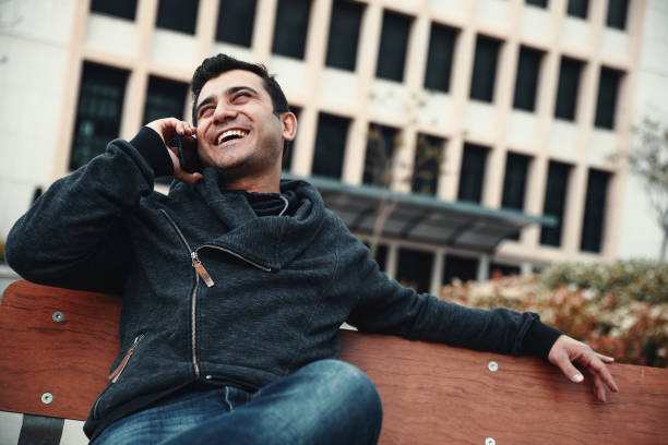 istock Young man on bench with talking mobile phone 945678424