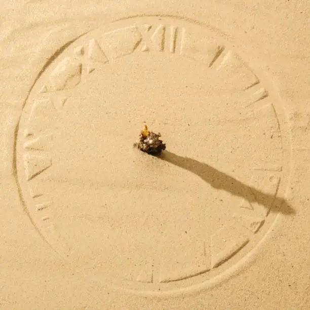 sun clock on sand with shadow and roman numbers