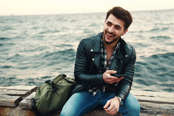 istock Young man sitting at coastline and talking on phone 945686260