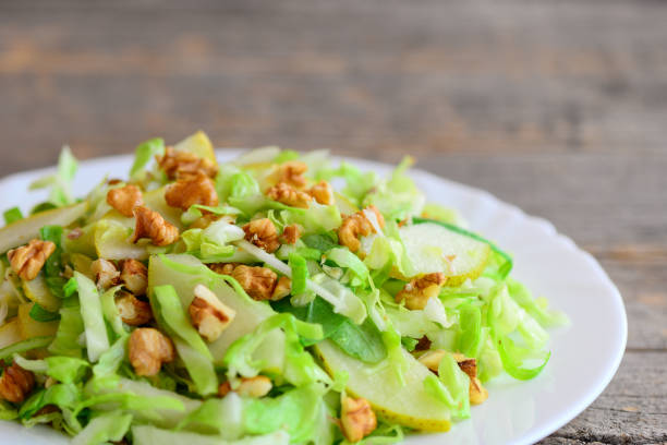 istock Pear cabbage slaw recipe. Simple salad with raw pear, cabbage and walnuts on a plate. Rustic wooden background. Clean eating. Closeup 945686450