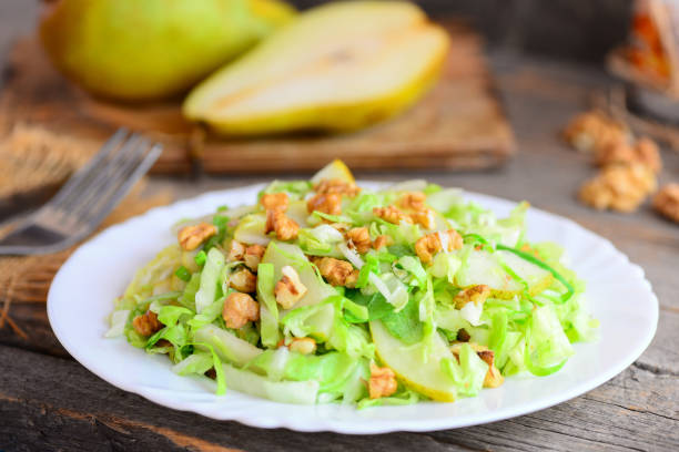 istock Pear and cabbage slaw. Home salad with fresh pear, cabbage and walnuts on a plate. Rustic wooden background. Easy healthy food. Closeup 945686476